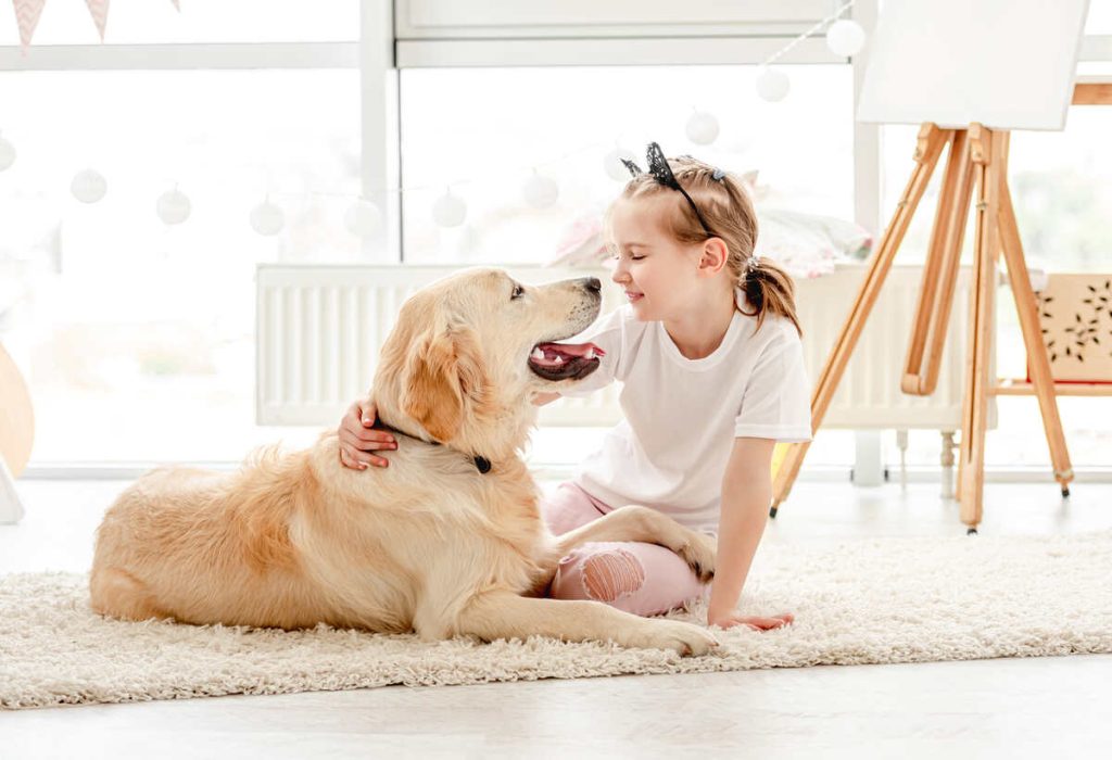 Cheerful little girl having fun with her dog in playroom